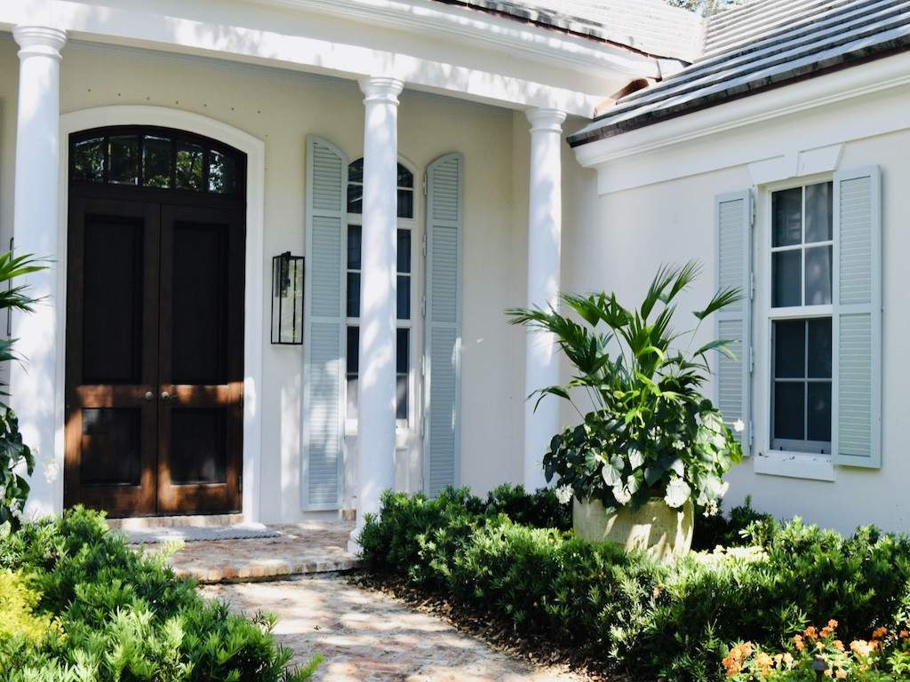 Mint green colonial shutters on off white house with white columns and a mahogany door