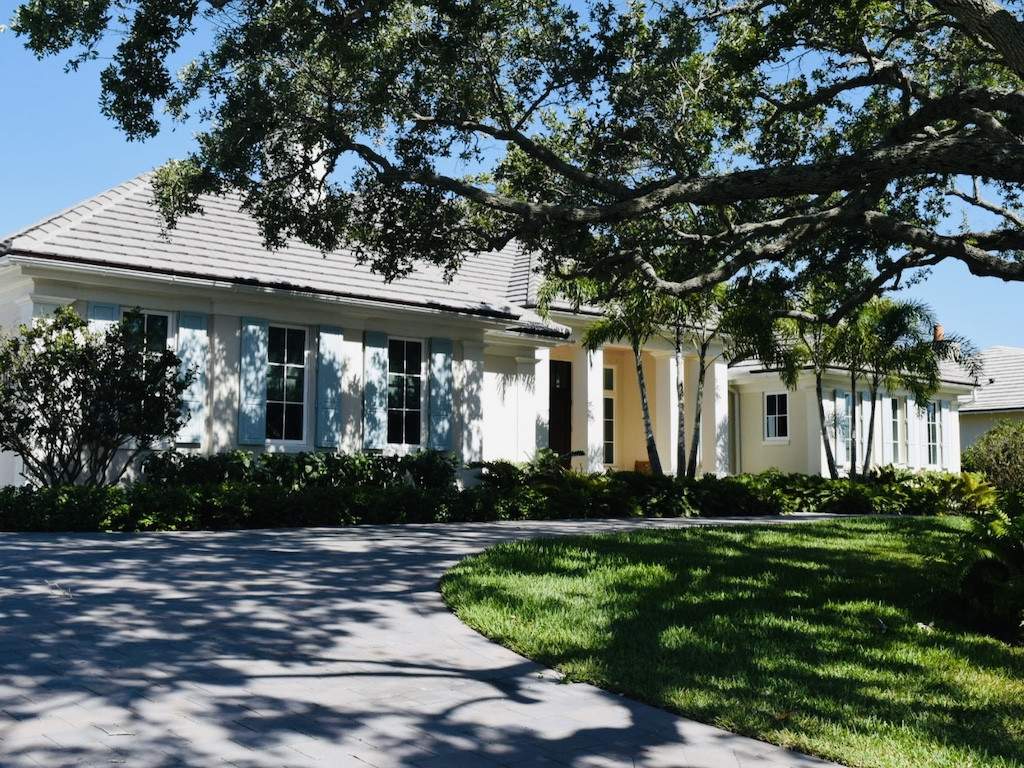 light blue colonial shutters on an off white house with a large oak tree in the front yard