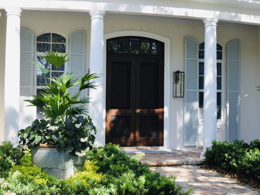 sage green colonial shutters on an off white house with a mahogany door